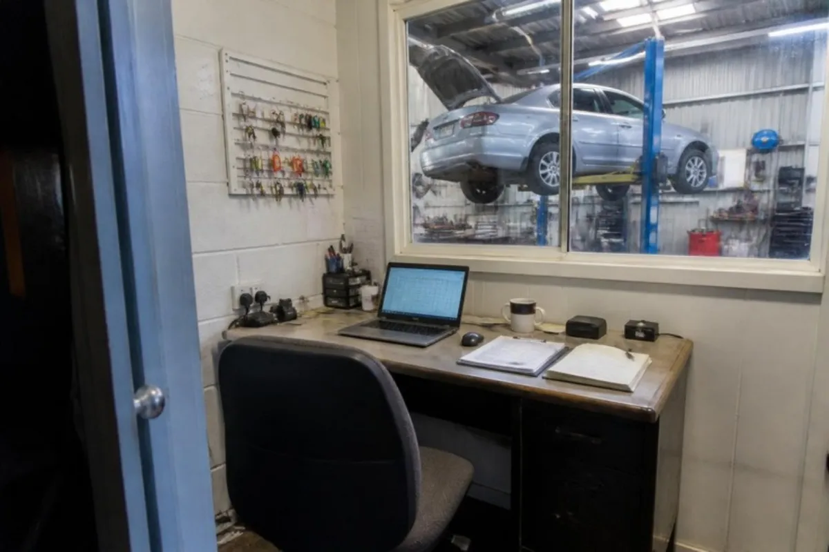 Small office overlooking a mechanic workshop with a laptop and job cards on the desk